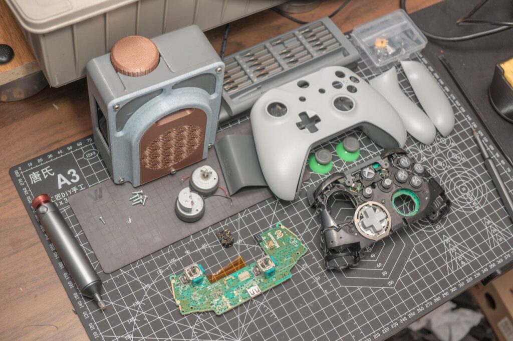 A disassembled video game controller and components set on a desk mat, illustrating electronics repair.
